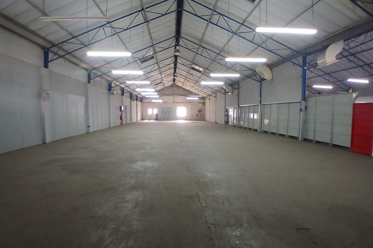 Spacious industrial warehouse featuring high exposed steel truss ceilings, concrete flooring, and functional overhead fluorescent lighting, suitable for various commercial or storage operations.