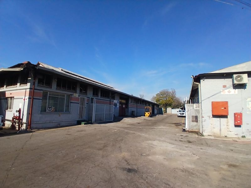 Industrial property exterior featuring a large asphalt yard, multiple warehouse access points, and functional utility infrastructure including external air conditioning units.