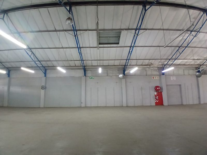 Spacious industrial warehouse interior featuring high ceilings with exposed steel trusses, concrete flooring, and functional overhead lighting.