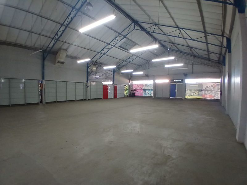 Spacious industrial warehouse unit featuring high exposed steel trusses, concrete flooring, and large glass storefront windows, suitable for various commercial or storage applications.
