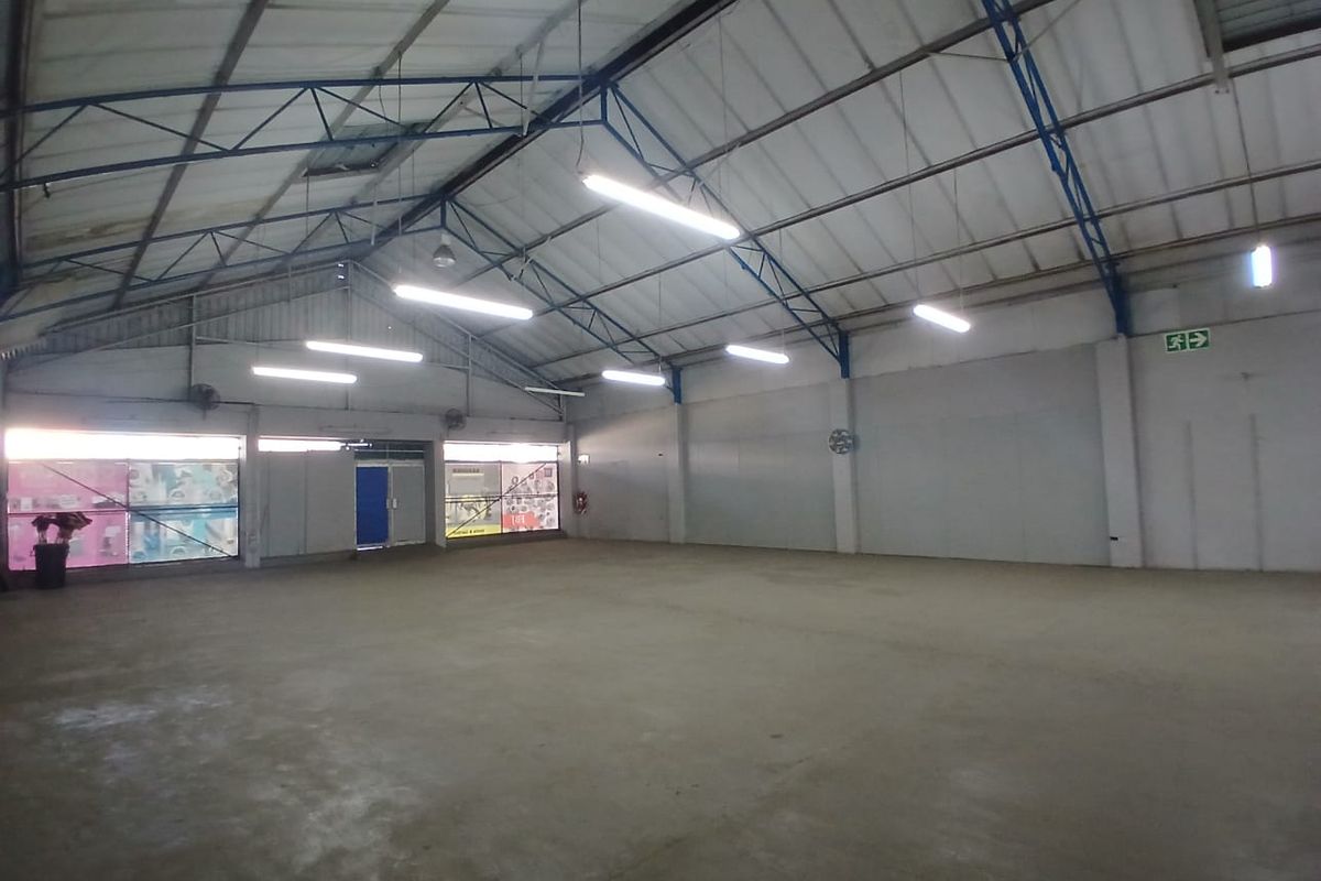 Spacious industrial utility area featuring high ceilings with exposed steel trusses, concrete flooring, and functional overhead fluorescent lighting.
