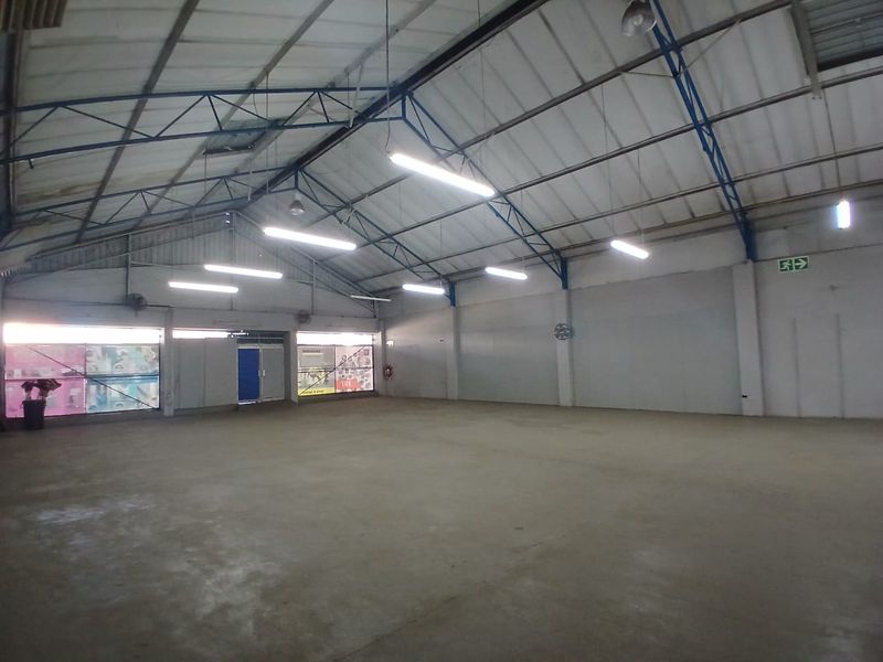 Spacious industrial utility area featuring high ceilings with exposed steel trusses, concrete flooring, and functional overhead fluorescent lighting.