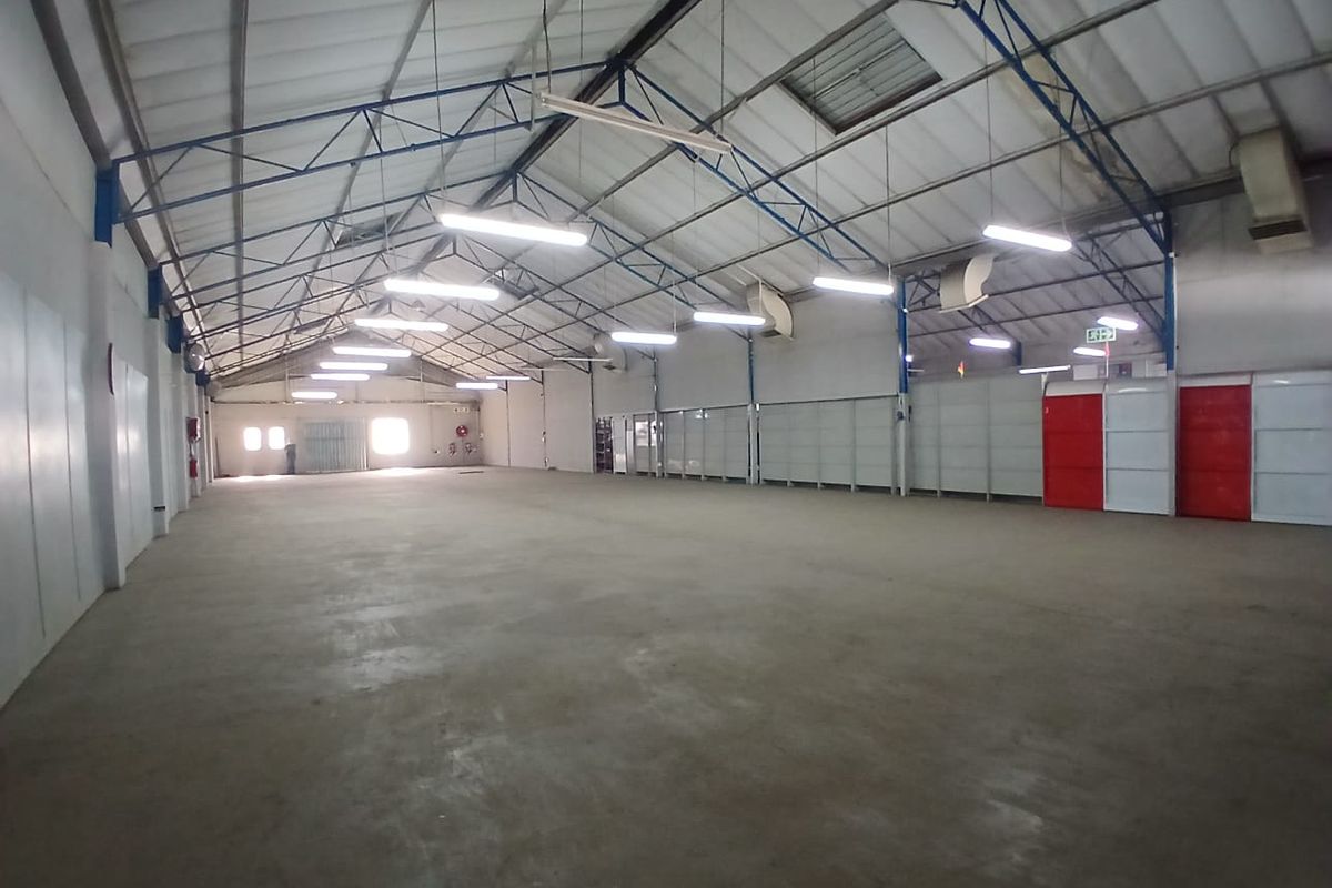 Spacious industrial warehouse unit featuring high ceilings with exposed steel trusses, concrete flooring, and ample overhead fluorescent lighting.