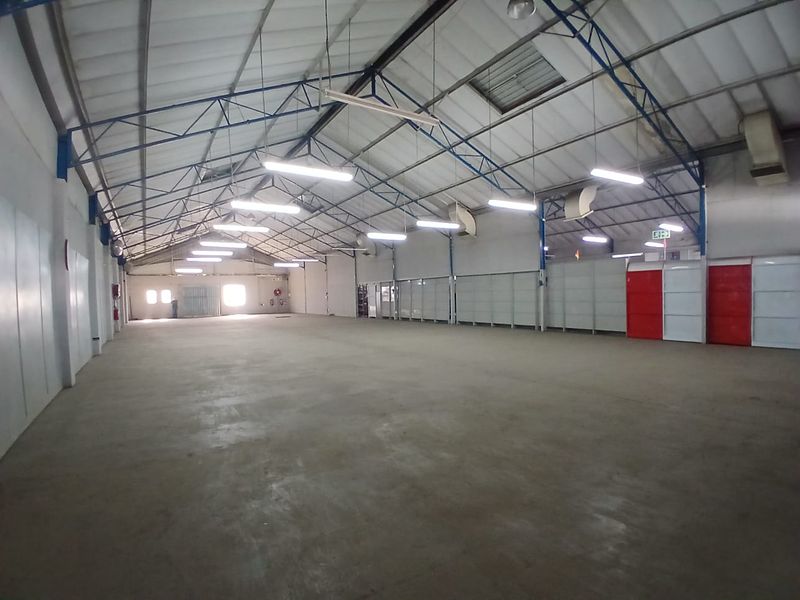 Spacious industrial warehouse unit featuring high ceilings with exposed steel trusses, concrete flooring, and ample overhead fluorescent lighting.