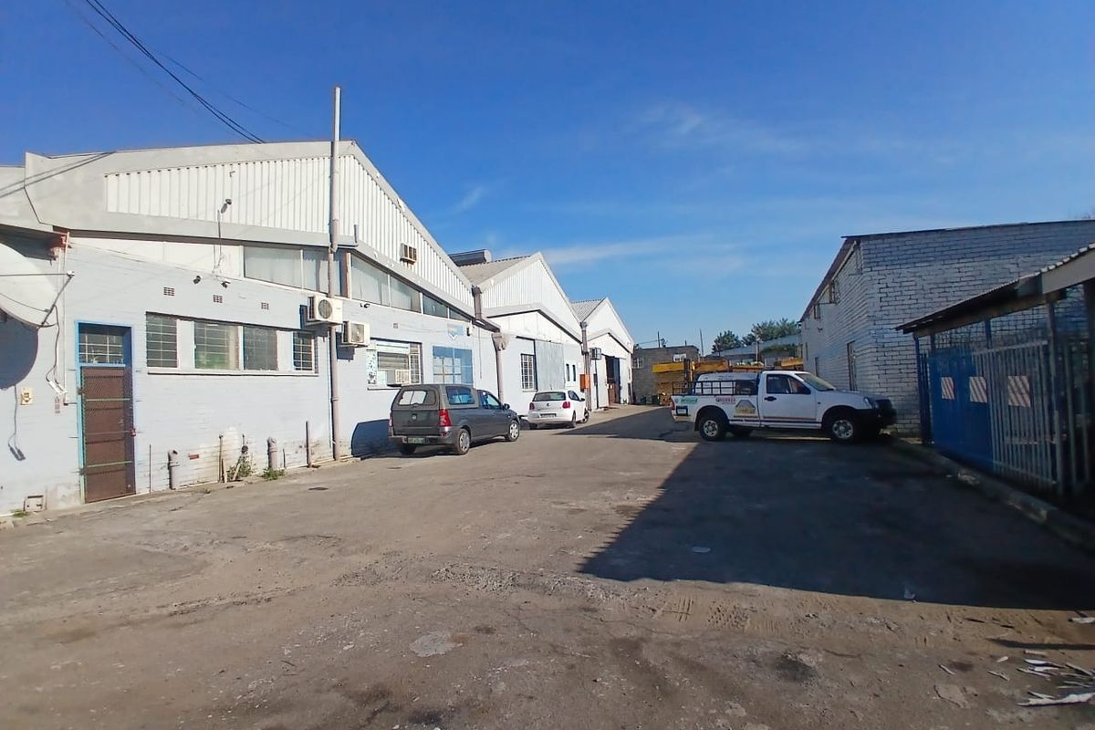 Exterior view of an industrial warehouse complex featuring a large asphalt yard and multiple building units with metal roofing.