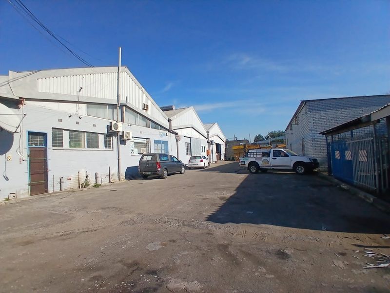 Exterior view of an industrial warehouse complex featuring a large asphalt yard and multiple building units with metal roofing.