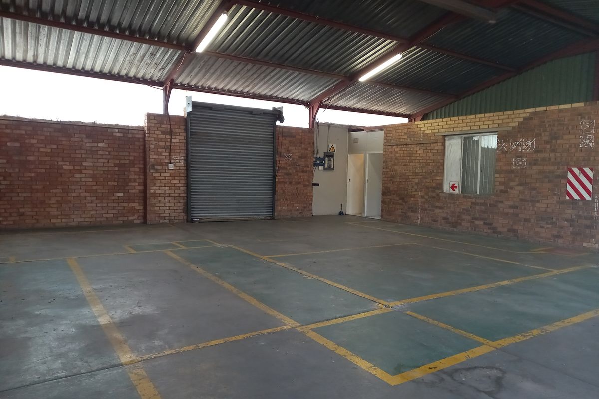 Spacious industrial warehouse unit featuring exposed brick walls, high-pitched corrugated metal roofing, a large roller shutter door, and painted concrete flooring.