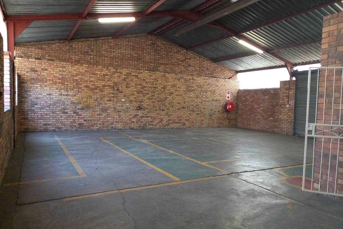 Spacious industrial garage or utility space featuring exposed brick walls, high-pitched corrugated metal roofing, and painted concrete flooring with marked bays.