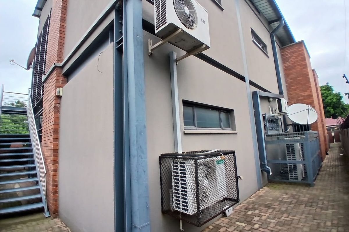 Exterior view of the office building side profile, featuring external air conditioning units, brick and plaster facade, and an external metal staircase.