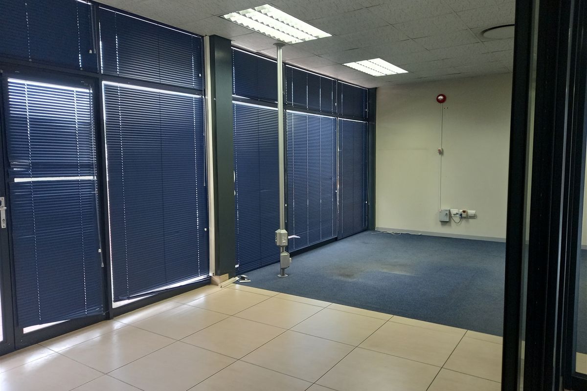 An empty office space featuring a mix of carpet and tile flooring, recessed lighting, and large windows with blue venetian blinds.