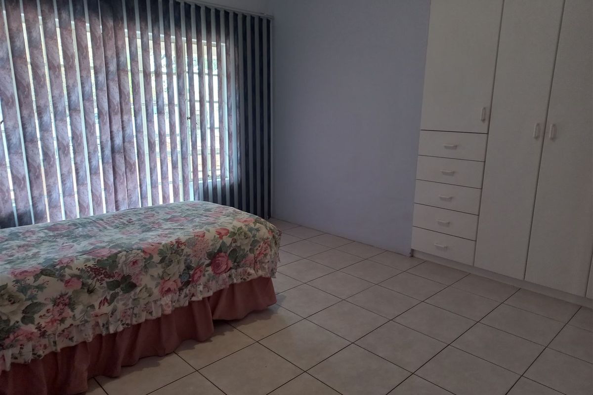 A bedroom featuring tiled flooring, built-in cupboards for storage, and vertical blinds covering the window.