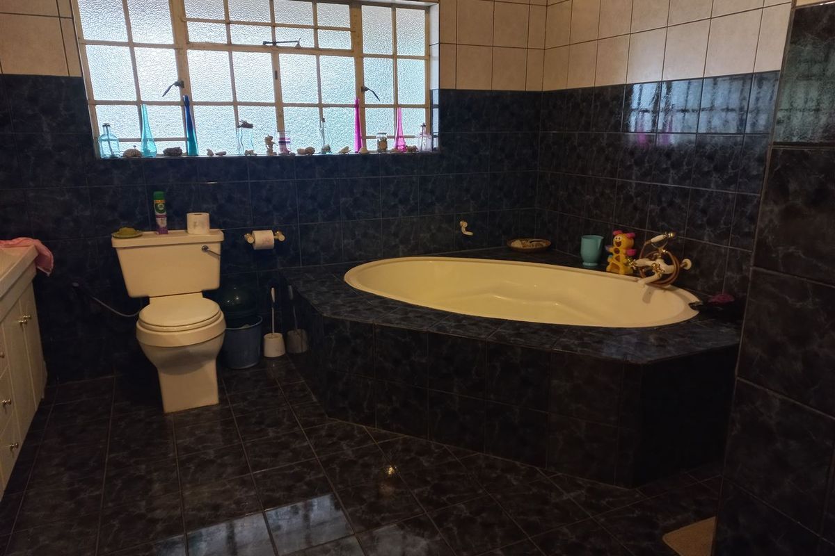 A functional bathroom featuring a built-in bathtub, toilet, and vanity cabinet with dark tiled finishes and natural light from a window.