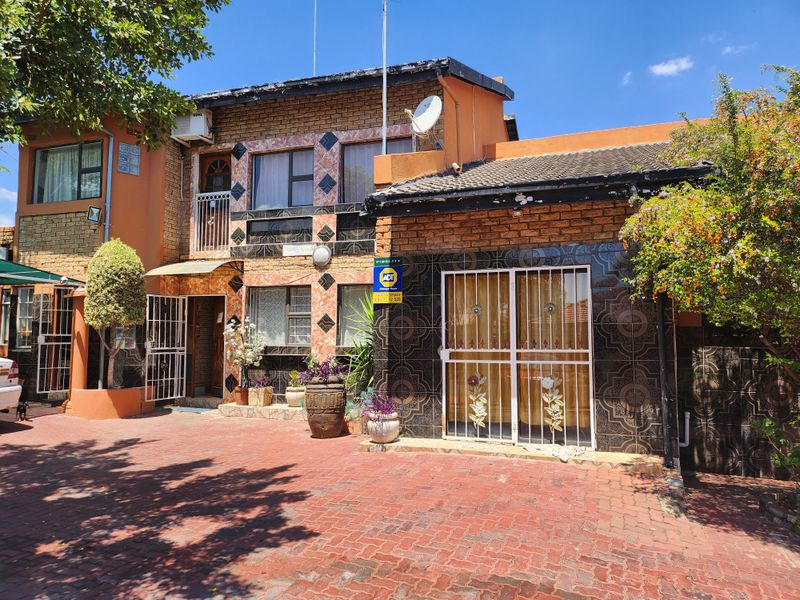 Front elevation of a two-story residential property featuring brick and tiled facade, paved driveway, and security gates.