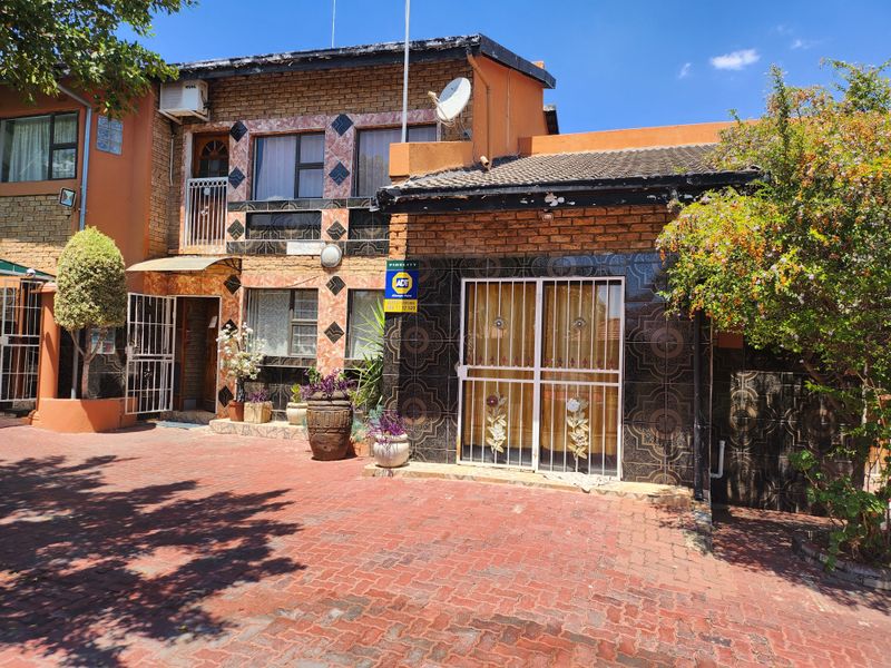 Front elevation of a multi-story residential property featuring brick and tiled facade, paved driveway, and security gates.
