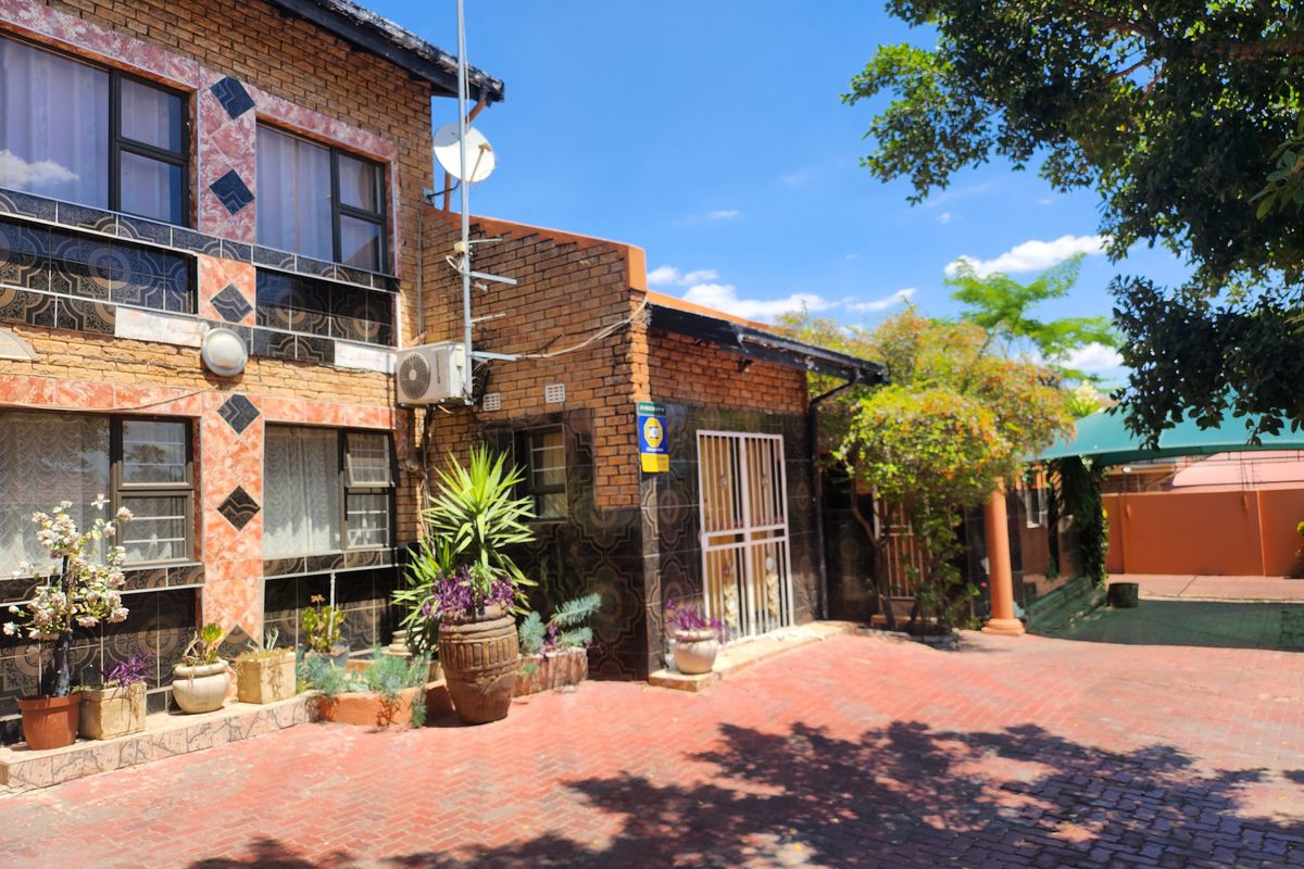 Front view of a double-story brick house featuring a paved driveway, security gate, and exterior wall tiling.