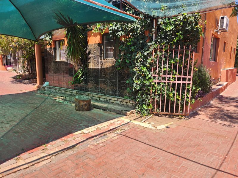 Outdoor patio area featuring brick paving, a shade sail, and decorative wall tiling, requiring some maintenance to the paving and surrounding vegetation.