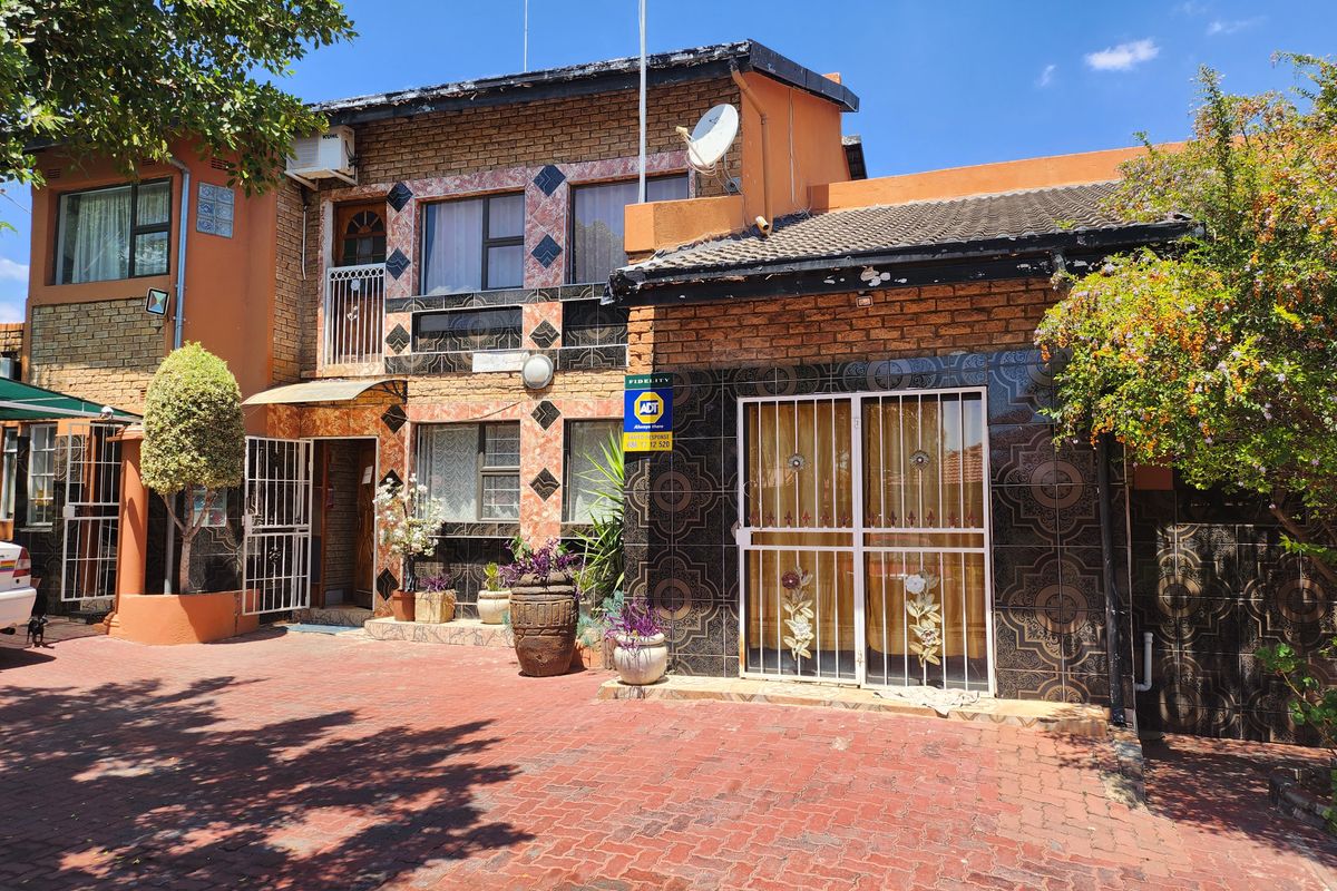Front elevation of a two-story residential property featuring brick and tiled facade, paved driveway, and security gates.