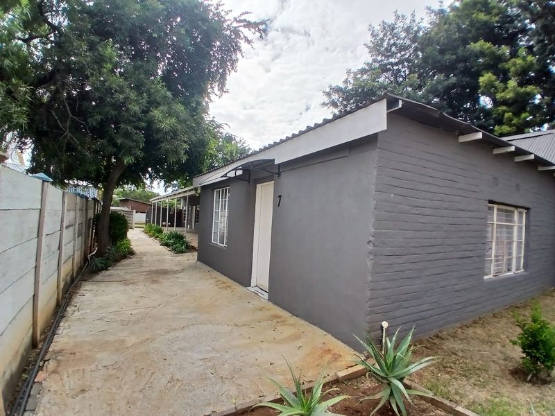 Side view of a painted brick residential building featuring a concrete pathway, steel window frames, and a precast concrete boundary wall.