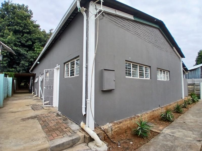 Rear exterior view of the property featuring grey painted walls, steel-framed windows, security gate, and paved access path.