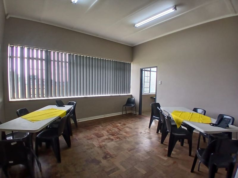 A functional office space featuring parquet flooring, large windows with vertical blinds, and overhead fluorescent lighting.