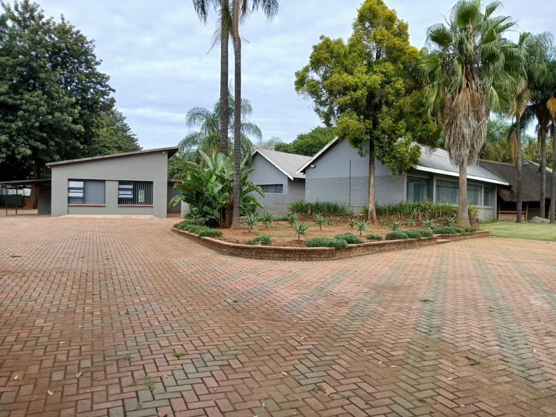 Front exterior view of the small holding featuring a large paved driveway, landscaped garden beds with brick retaining walls, and multiple building structures.