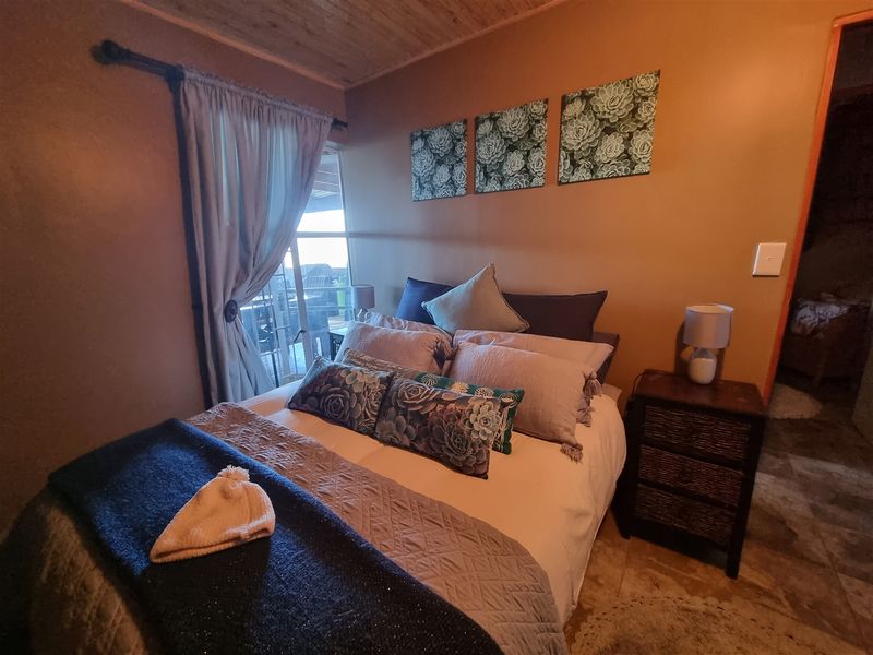 A cozy bedroom featuring a timber-clad ceiling, tiled flooring, and a sliding glass door providing access to an outdoor area.