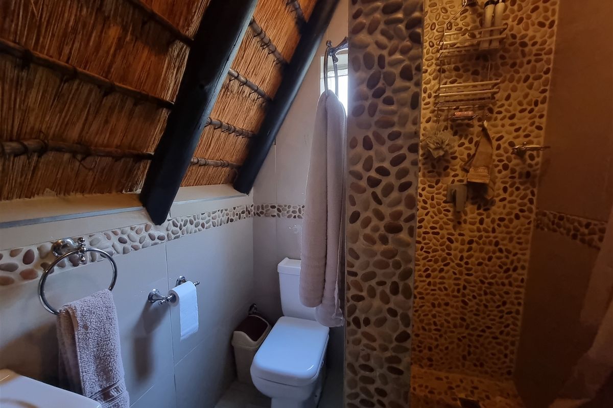A unique bathroom featuring a rustic thatched roof, pebble-tiled shower enclosure, and standard sanitary fixtures in a compact layout.