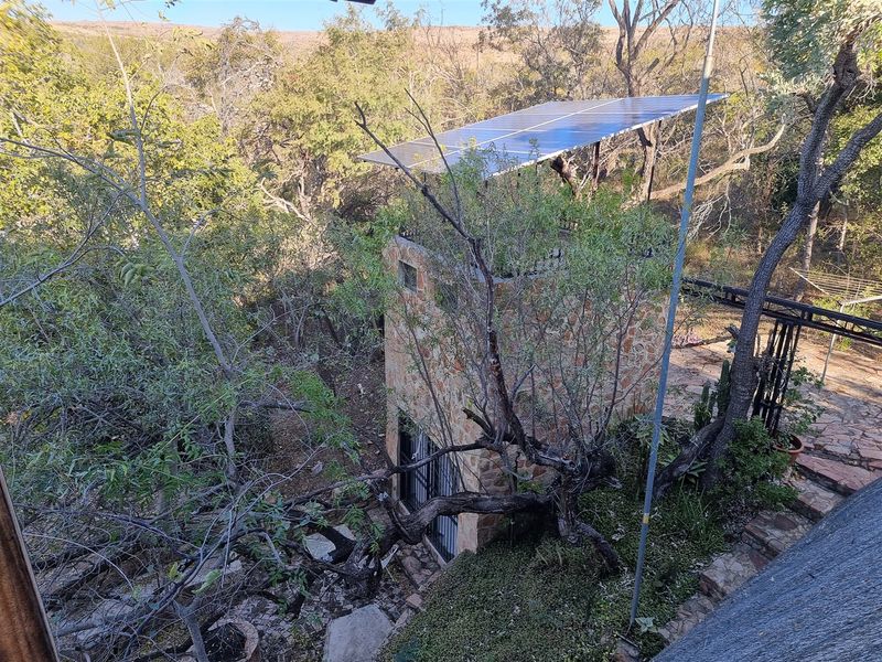 An elevated view of a stone-clad structure featuring roof-mounted solar panels, surrounded by mature trees and natural landscaping.