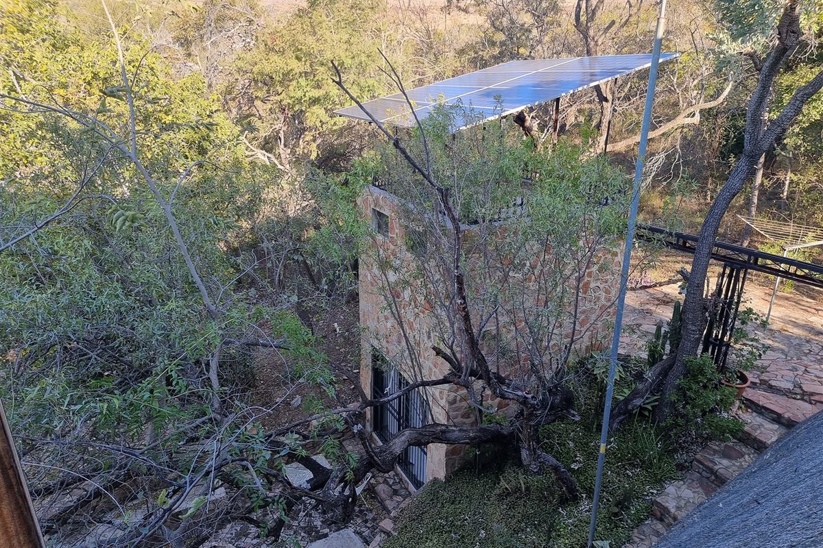 An elevated view of a stone-clad structure featuring roof-mounted solar panels, surrounded by mature trees and natural landscaping.