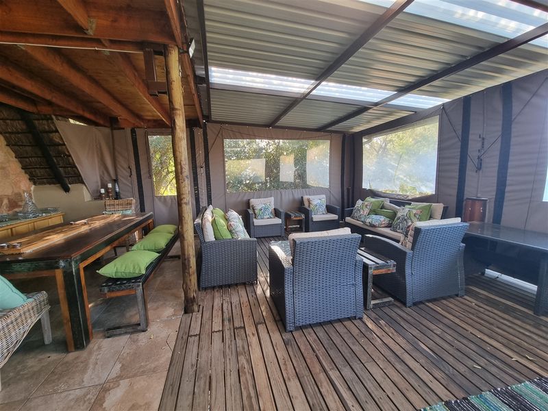 A spacious covered outdoor patio featuring timber decking, stone flooring, and a corrugated roof with translucent panels, ideal for relaxed outdoor entertaining.
