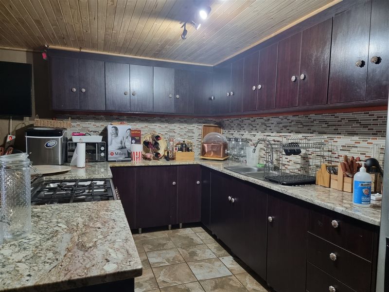 A functional kitchen featuring dark wood cabinetry, granite countertops, a mosaic tile backsplash, and a timber tongue and groove ceiling.