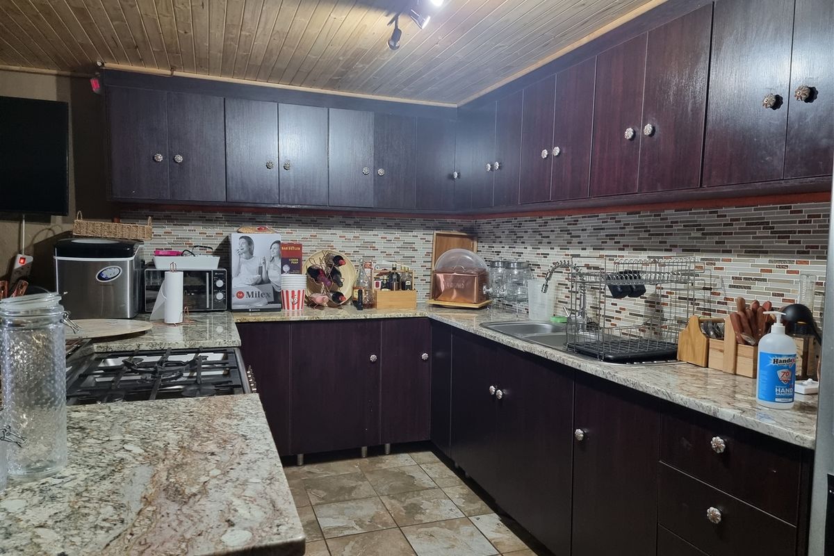 A functional kitchen featuring dark wood cabinetry, granite countertops, a mosaic tile backsplash, and a timber tongue and groove ceiling.
