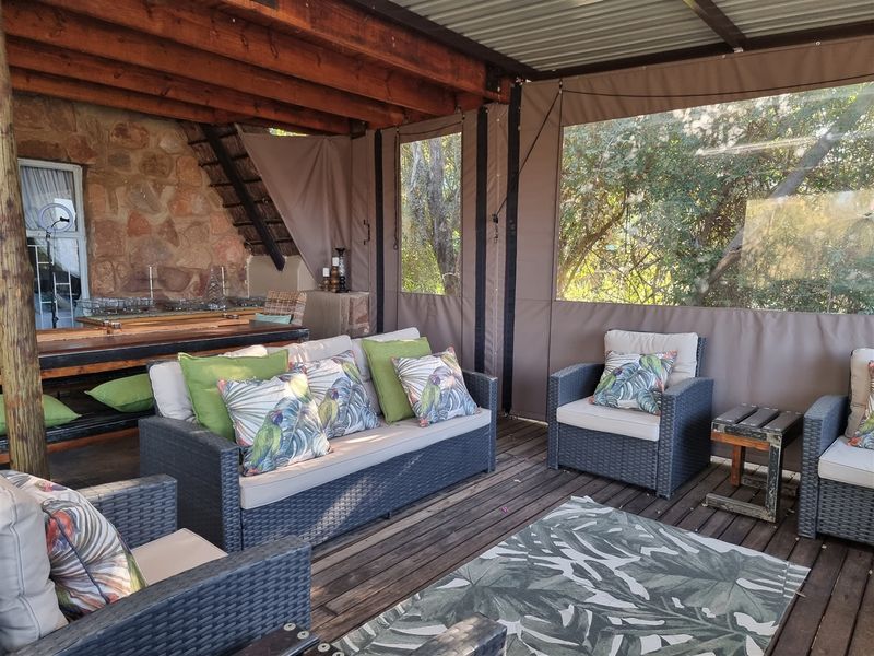 A covered outdoor patio featuring timber decking, a rustic stone feature wall, exposed timber beams, and protective canvas roll-up blinds.