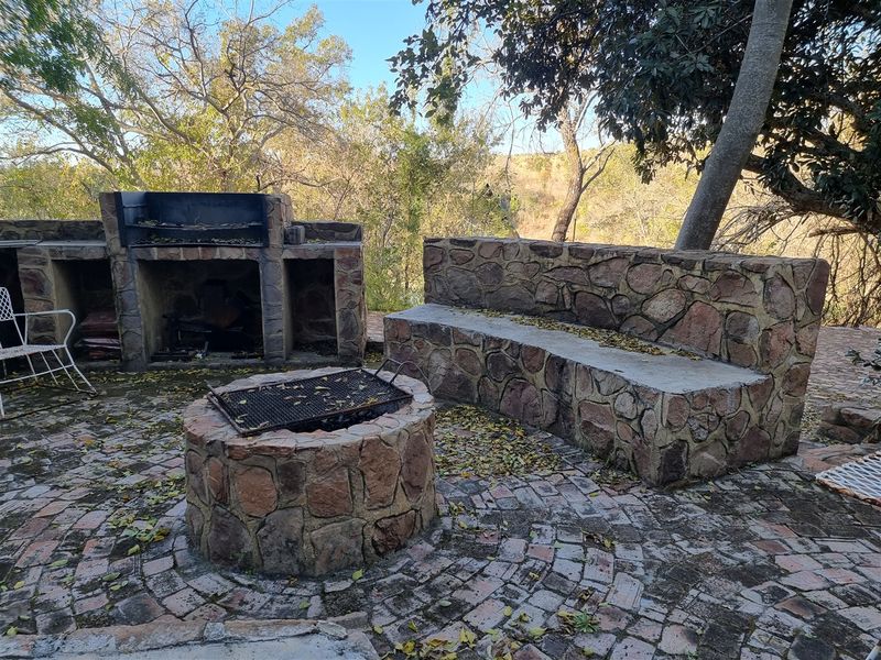 Outdoor entertainment area featuring a built-in stone braai, a circular stone fire pit, and a stone bench set on brick paving.