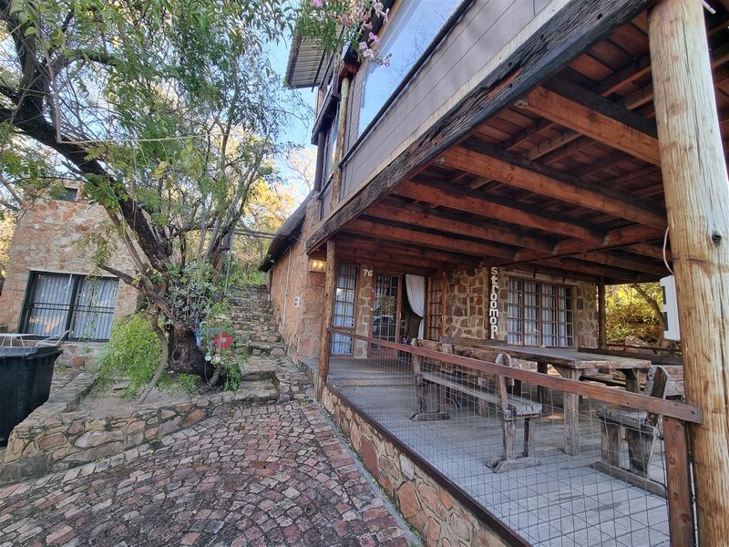 A rustic covered patio area featuring exposed timber beams, stone wall cladding, and direct access to a stone-paved garden path.