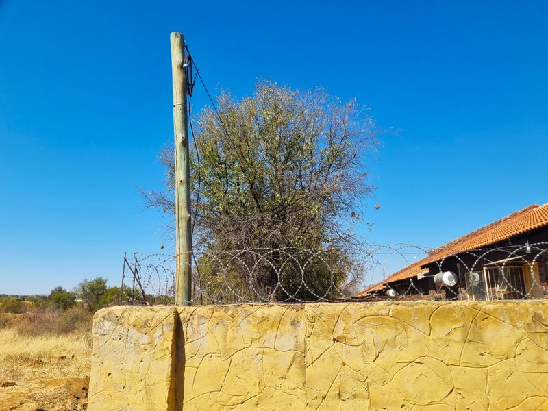 View of a residential boundary wall featuring razor wire security fencing, a utility pole, and a portion of a tiled roof structure.