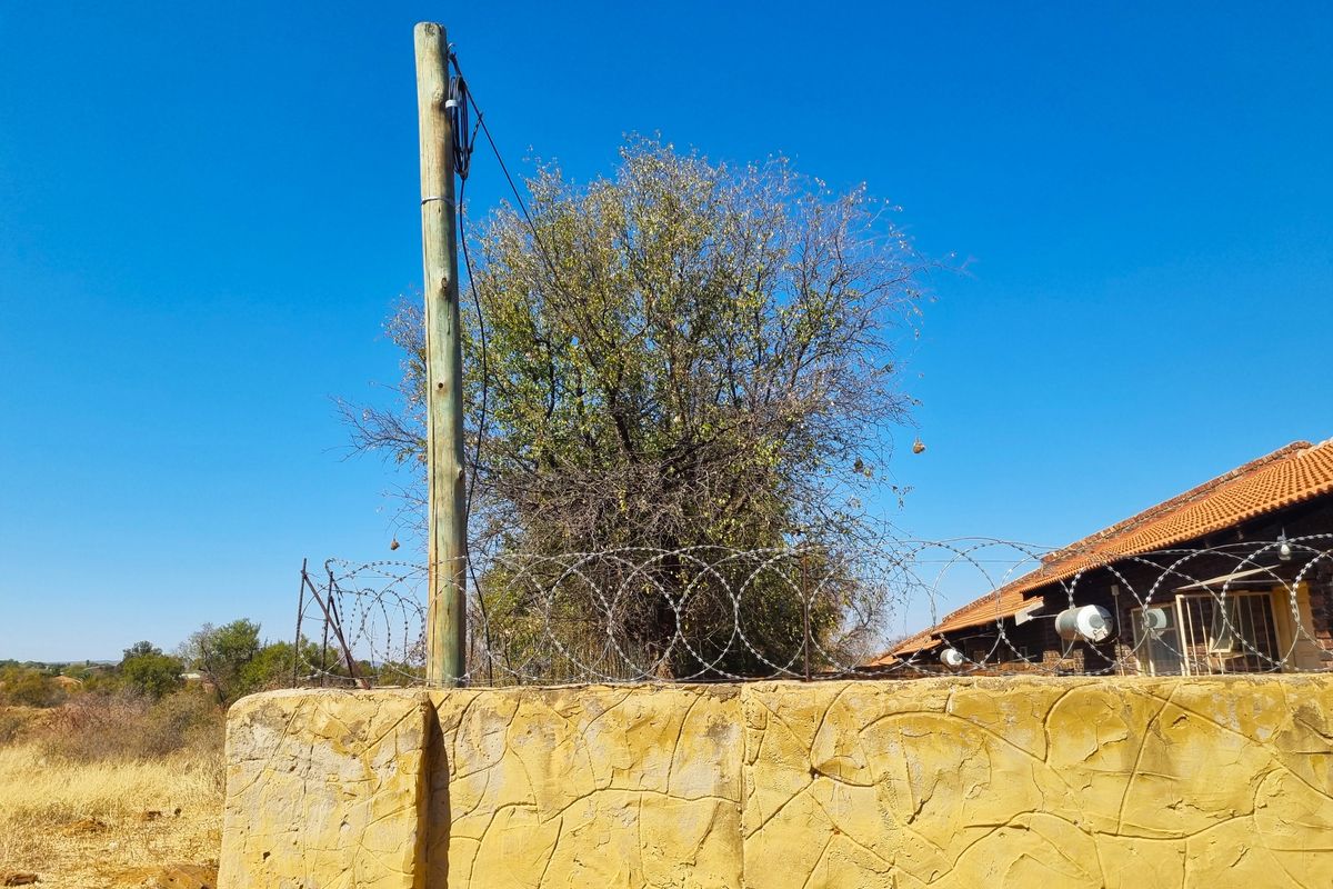 View of a residential boundary wall featuring razor wire security fencing, a utility pole, and a portion of a tiled roof structure.