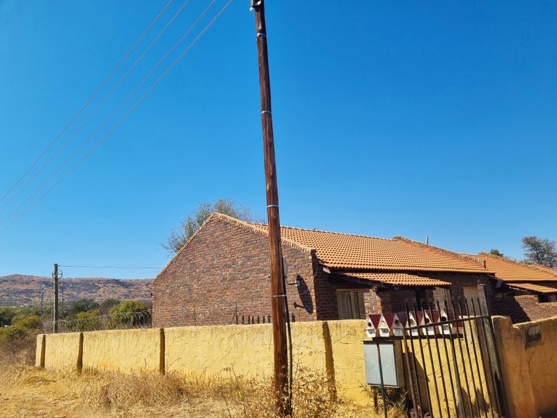 Front exterior view of a face brick residential property featuring a tiled roof, perimeter wall with security fencing, and gated access.