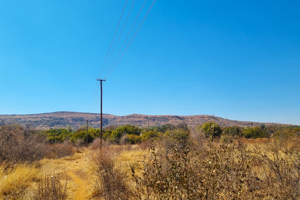 A view of the vacant residential land featuring natural dry vegetation, utility poles, and distant mountain scenery under a clear blue sky.