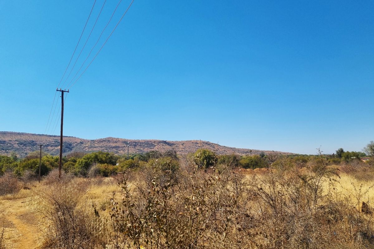 A view of the vacant residential land featuring natural vegetation, a utility pole, and distant mountain scenery under a clear blue sky.