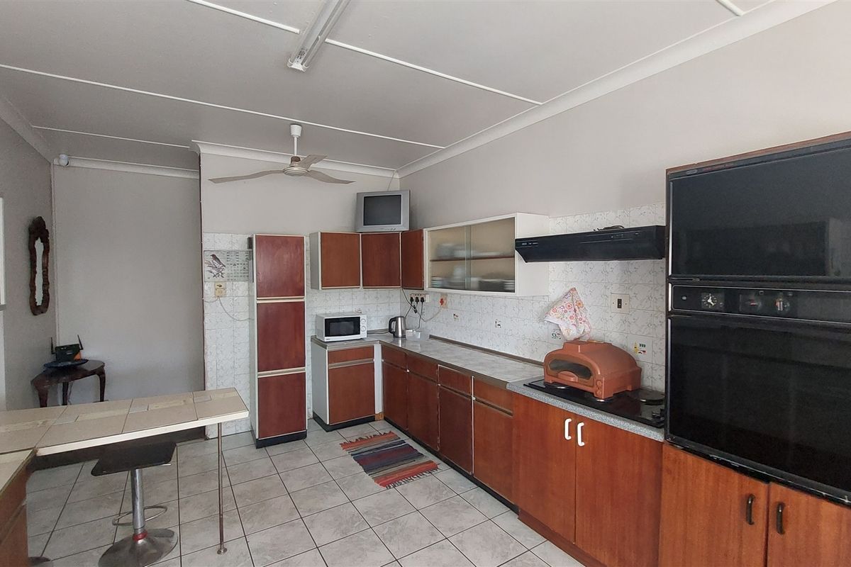 A functional kitchen featuring dated wood-finish cabinetry, a double wall oven, extractor fan, and tiled flooring with a breakfast counter area.