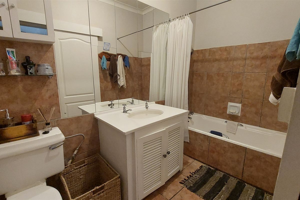 A functional bathroom featuring a vanity cabinet with integrated sink, large wall mirror, bathtub with shower curtain, and tiled wall and floor finishes.