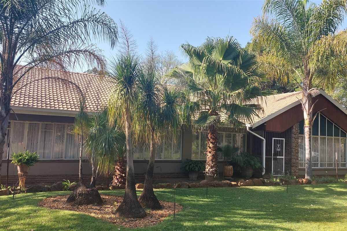 A view of the rear elevation of the house featuring a tiled roof, brick exterior, and a well-maintained garden with mature palm trees.