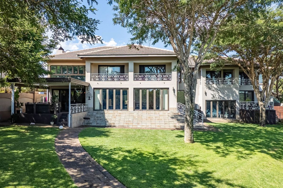 Spacious rear elevation of a two-story house featuring a large landscaped garden, paved walkway, tiled patio, and elegant wrought iron balcony railings.