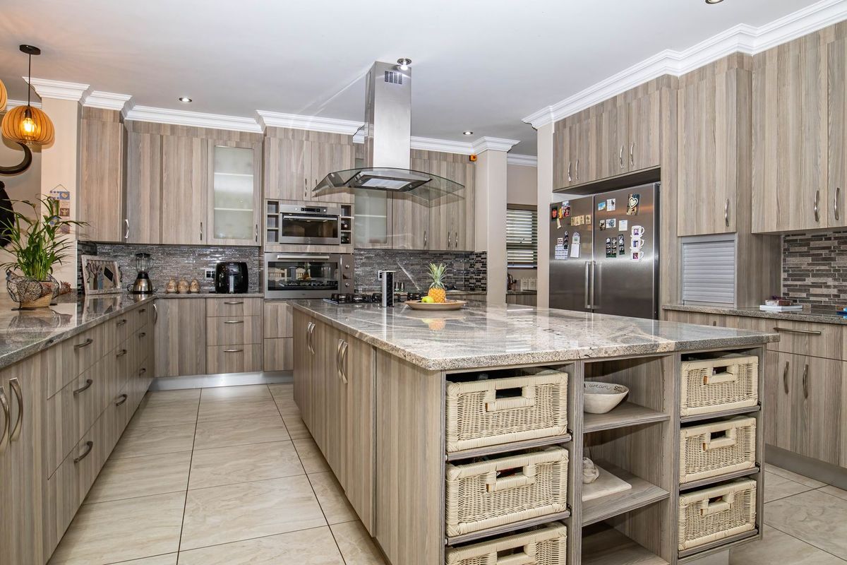 Modern kitchen featuring a large central island, granite countertops, built-in appliances, mosaic tile backsplash, and ample cabinetry with a neutral wood-grain finish.