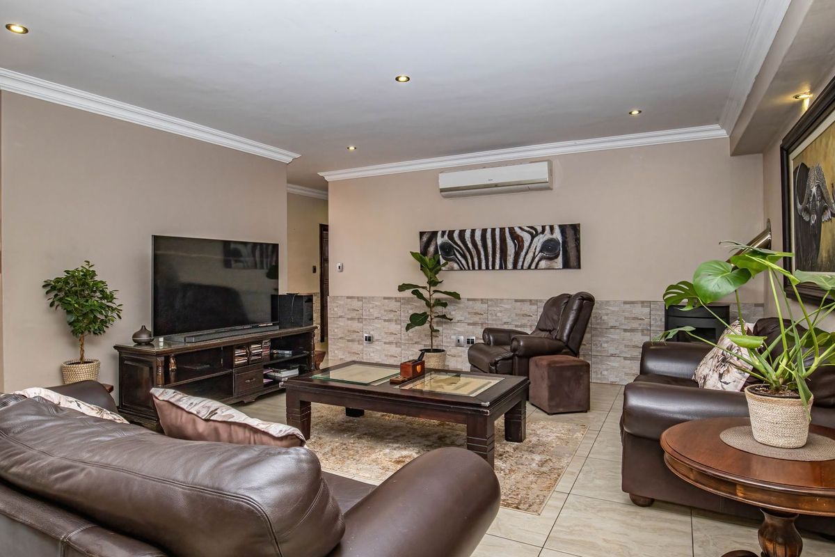 Spacious living room featuring tiled flooring, recessed downlighting, crown molding, and a wall-mounted split-system air conditioner.