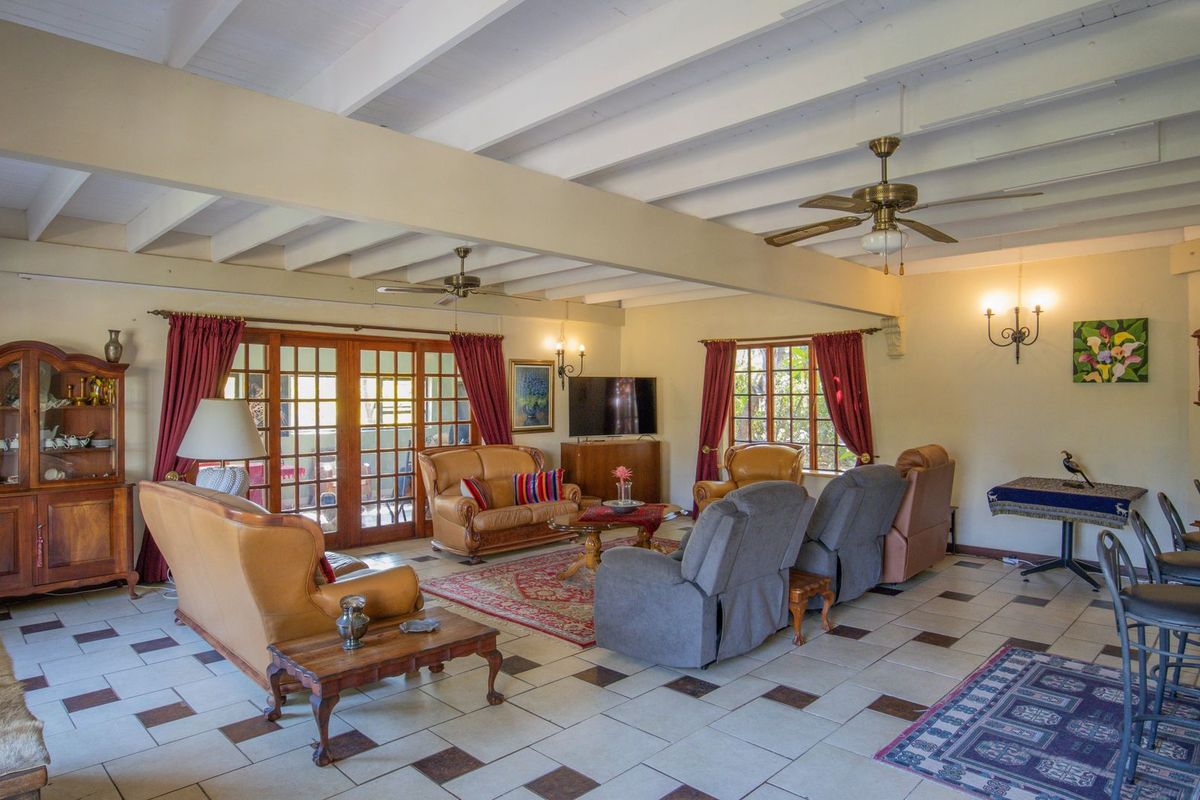 Spacious living room featuring exposed beam ceilings, ceiling fans, tiled flooring, and large french doors providing access to the outdoor area.