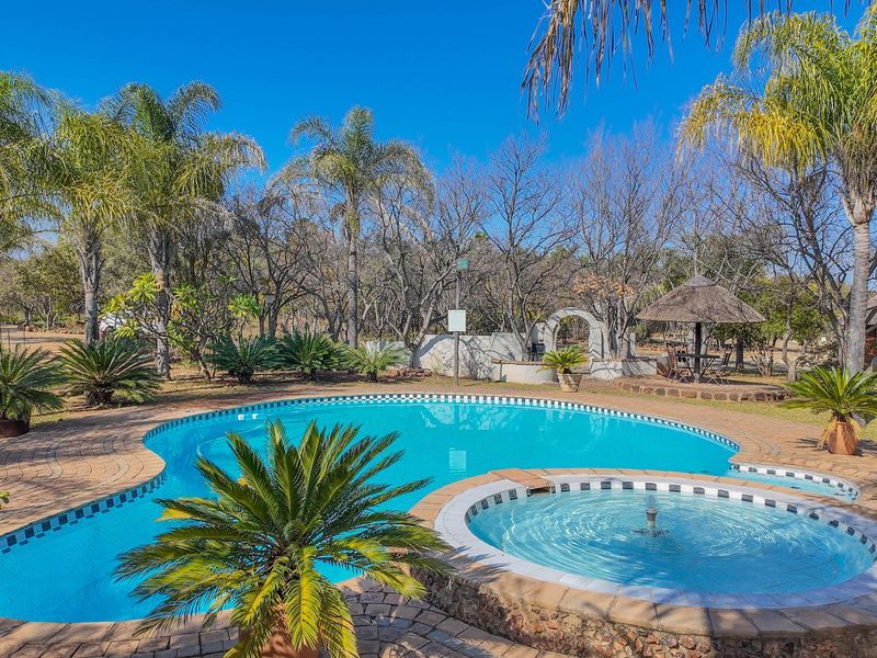 Outdoor pool area featuring a swimming pool with an integrated spa, paved surround, and a thatched gazebo set within a landscaped garden.