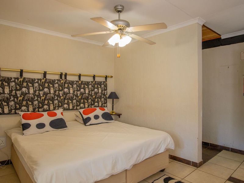 A bedroom featuring tiled flooring, a ceiling fan, and a wooden door leading to an adjacent area with a fire extinguisher.