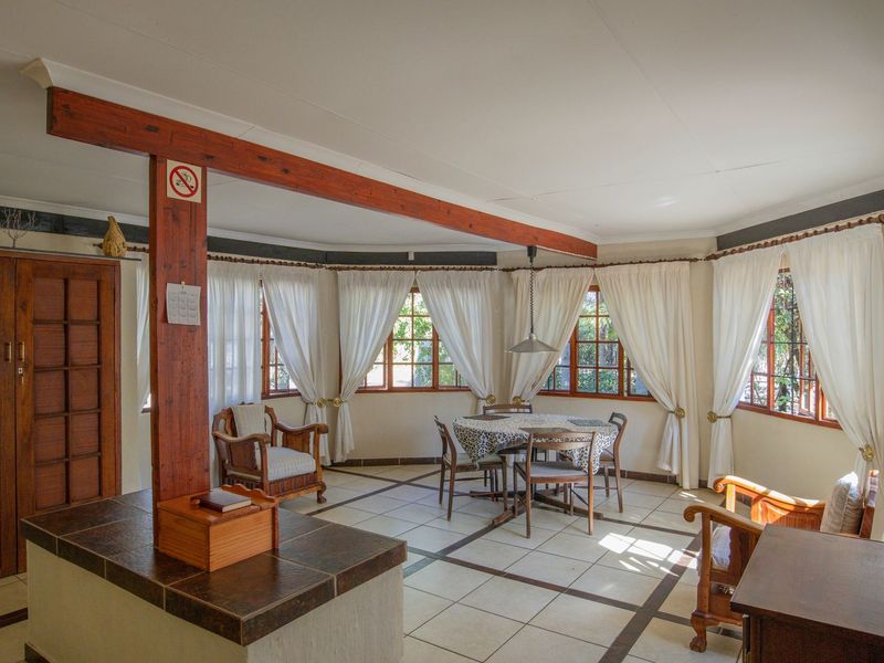 Spacious open-plan living and dining area featuring exposed timber beams, large windows, and tiled flooring, offering a bright and functional layout.